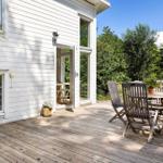 Terrasse mit Holztisch und Stühlen neben weißem Haus mit Fenstern.