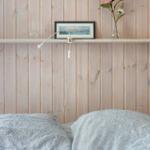 Schlafzimmer mit Holzwand, Bett und Regal mit Bild und Blumen.