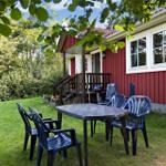 Red wooden house with porch and garden furniture under trees.