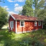 Red wooden house with white windows and roof surrounded by trees.