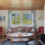 Living room with sofa, table and fireplace. Windows show green trees.