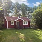 Red vacation house with terrace and garden in green surroundings.