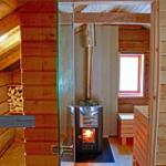 Sauna with wood stove, bench, and window. Wooden walls and roof structure visible.