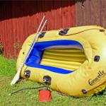Yellow inflatable boat with oar and pump on grass near wooden wall