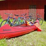 Red canoe and bicycles in front of red wooden shed on grass