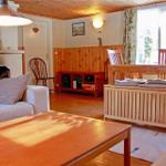 Living room with sofa, coffee table, and dining table. Wooden walls and window with curtains.