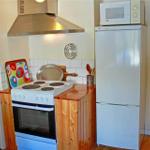 Kitchen with stove, refrigerator, and microwave. Wooden surfaces and white tiles.
