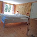 Bedroom with wooden walls, white bed, and window with view of forest.