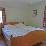 Double bed with white bedding, wooden floor, and two windows with red curtains.