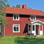 Red wooden house with white windows and porch. Surrounded by greenery with picnic table.