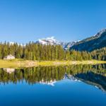 Hütte am See mit Bergspitze und Waldreflexion.