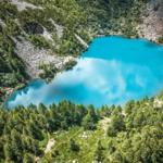 Ein tiefblauer See liegt inmitten grüner Berghänge und Wälder.