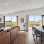 Wohn- und Essbereich mit braunem Sofa, Tisch und großen Fenstern zur Landschaft.