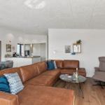 Wohnzimmer mit braunem Sofa, Esstisch und Küche im Hintergrund.