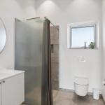 Badezimmer mit Dusche, Waschbecken und Toilette. Fenster mit Pflanze.