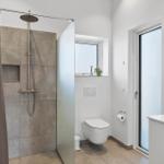Badezimmer mit Dusche, WC und Waschtisch. Fenster und Spiegel sichtbar.