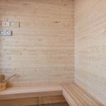 Sauna mit Holzwand, Sitzbank und Eimer mit Löffel.
