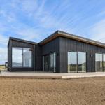 Moderne Villa mit großzügigen Glasflächen und Holzterrasse im Freien.