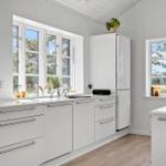 Küche mit weißen Schränken, Fenstern und Holzboden. Auf der Arbeitsplatte steht eine Weinflasche.