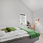 Schlafzimmer mit Bett, grünen Kissen und Decke, Fenster, Pflanzen und Wandlampe.