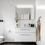 Badezimmer mit Waschbecken, Spiegel und Toilette. Handtuch hängt an Wand.