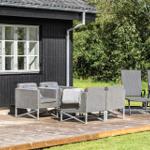 Terrasse mit Sitzgruppe und Liegestühlen vor schwarzem Holzhaus mit grünem Hintergrund.