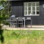 Terrasse mit Tisch, Stühlen und Grill vor schwarzem Holzhaus.