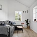 Wohnzimmer mit grauem Sofa, Holzboden und großen Fenstern. Wanddekoration und Pflanzen.