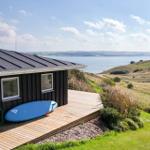 Haus mit Holzterrasse und Blick aufs Wasser. Blauer Surfbrett liegt bereit.