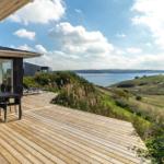 Terrasse mit Tisch und Stühlen bietet Blick auf See und Hügel.