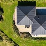 Haus mit schwarzem Dach und umliegenden Grünflächen von oben gesehen.