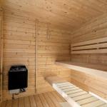 Sauna mit Holzwand, Bänken und Heizung. Fenster zeigt grüne Vegetation.
