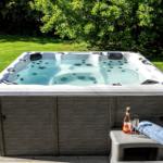 Hochwertige Whirlpool mit Getränk und Handtuch auf Holzterrasse im Grünen.