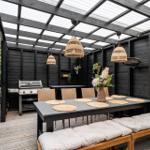 Gartenbereich mit Grill, Esstisch und Sitzbank unter Dach.