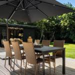 Terrasse mit Tisch, Stühlen und Sonnenschirm. Hintergrund: Garten und Holzhaus.