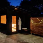Sauna mit Holzverkleidung und Lichterkette auf Terrasse bei Nacht.