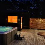 Außenbereich mit Whirlpool, Sauna und Liegen auf Holzterrasse bei Nacht.