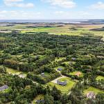 Luftbild einer ländlichen Gegend mit Wäldern, Häusern und Blick aufs Meer.