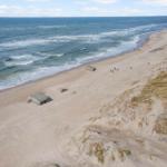 Strand mit Dünen, Wellen und historischen Bunkern.