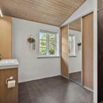 Badezimmer mit Holzdecke, Waschbecken, Dusche und Fenster mit Blick auf Grün.