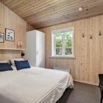 Schlafzimmer mit Holzwänden, Bett, Kleiderständer und Fenster.