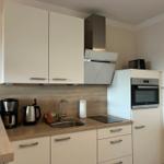 Küche mit weißen Schränken, Edelstahlspüle und integriertem Backofen.