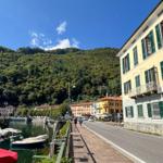 Street along the harbor with boats and green hills in the background.