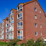 Red brick building with white windows and balconies under blue sky.