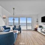 Wohnzimmer mit Blick aufs Wasser, blauer Sofa, TV und Stehregal.