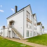 Modernes Haus mit Terrasse und Stufen zur Eingangstür. Grünfläche und Wasser im Hintergrund.