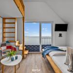 Schlafzimmer mit Blick aufs Wasser, Bett, TV und Holztreppe.