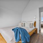 Schlafzimmer mit Holzbett, blauer Decke und Blick in angrenzenden Raum.