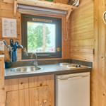 Küche mit Spüle, Herd und Kühlschrank. Holzwände und Fensterblick.