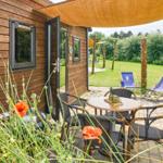 Terrasse mit Tisch, Stühlen und Sonnensegel. Rotes Mohnblumenfeld im Vordergrund.